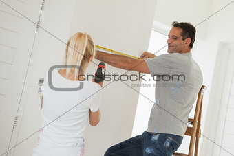 Woman holding drill while man measuring wall