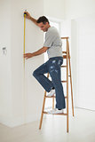 Full length of a man on ladder while measuring wall