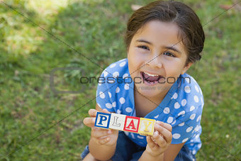 Happy girl holding block alphabets as \'play\' at park