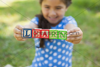 Happy girl holding block alphabets as 'learn' at park