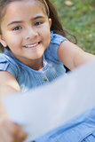 Smiling girl holding out a blurred paper at park