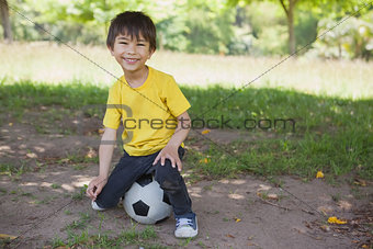 Portrait of a cute boy sitting on football at park