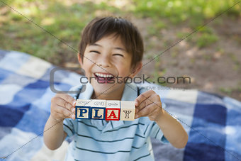 Happy boy holding block alphabets as 'play' at park