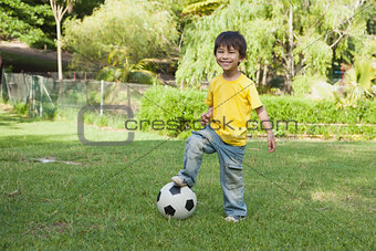 Cute little boy with football standing at park