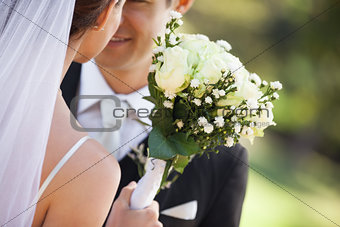 Mid section of a newlywed couple with bouquet in park