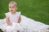 Baby with stuffed toy sitting on blanket at park