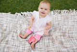 Cute baby with heart shaped lollipop sitting on blanket at park
