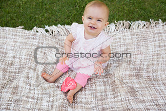 Cute baby with heart shaped lollipop sitting on blanket at park