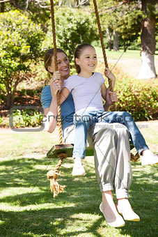 Happy mother and daughter sitting on swing at park