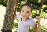 Happy young girl sitting on swing at park