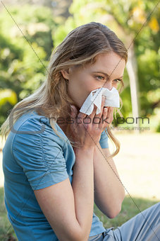 Woman blowing nose with tissue paper at park