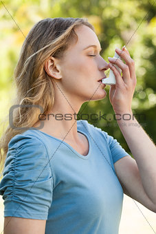 Young woman using asthma inhaler at park
