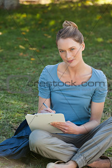 Relaxed young woman writing on clipboard at park