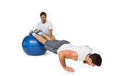 Male trainer helping young man exercise on fitness ball