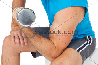 Mid section of a fit man exercising with dumbbell