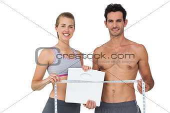 Sporty couple holding scales and measuring tape