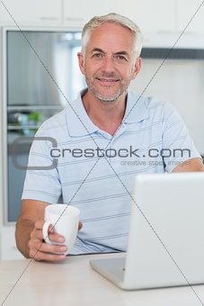 Casual smiling man using his laptop while having coffee