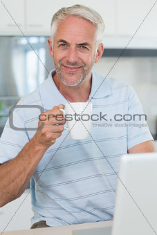 Smiling man using his laptop while having coffee