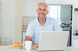 Happy man using his laptop at breakfast