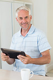 Smiling man using his tablet at breakfast