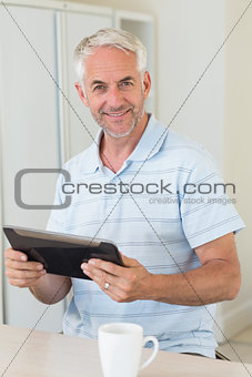 Smiling man using his tablet at breakfast