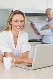 Happy woman using laptop with partner standing with the paper