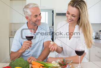 Cheerful couple making dinner together and drinking red wine
