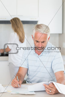 Worried man working out finances with partner standing behind