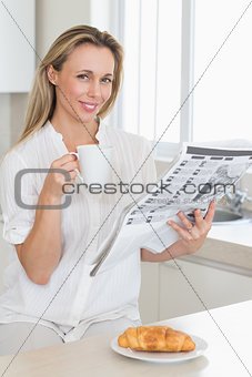 Happy woman holding mug and newspaper at breakfast