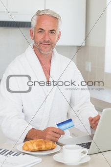 Happy man shopping online at breakfast in a bathrobe