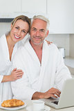 Smiling couple using laptop at breakfast in bathrobes