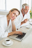 Couple having coffee at breakfast in bathrobes using laptop