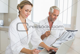 Couple shopping online and reading newspaper in bathrobes