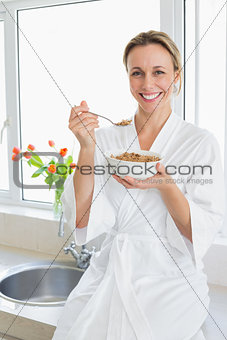 Smiling woman in bathrobe having cereal