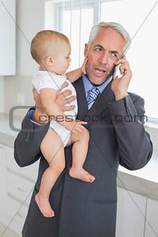 Distracted businessman holding his baby in the morning before work