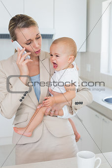 Businesswoman holding her crying baby talking on the phone