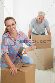 Happy couple sealing cardboard moving boxes