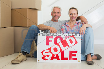 Happy couple sitting on floor with sold sign