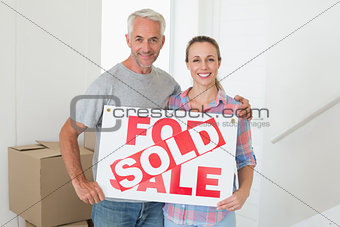 Happy couple standing and holding sold sign