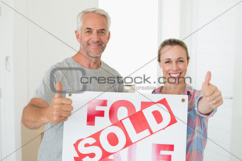 Happy couple standing and holding sold sign giving thumbs up