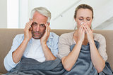 Sick couple sitting on the couch under a blanket