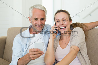 Happy couple sitting on couch talking and texting on their phones