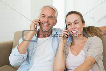 Happy couple sitting on couch talking on their phones