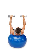 Young man exercising with dumbbells on fitness ball