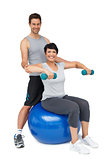 Male trainer assisting woman with dumbbells