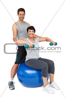 Male trainer assisting woman with dumbbells