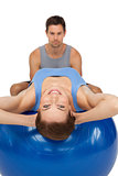 Male trainer helping young woman stretch on fitness ball