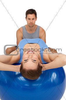 Male trainer helping young woman stretch on fitness ball