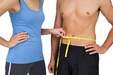 Mid section of a fit woman measuring mans waist