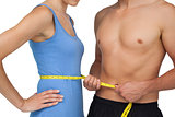 Mid section of a fit man measuring womans waist